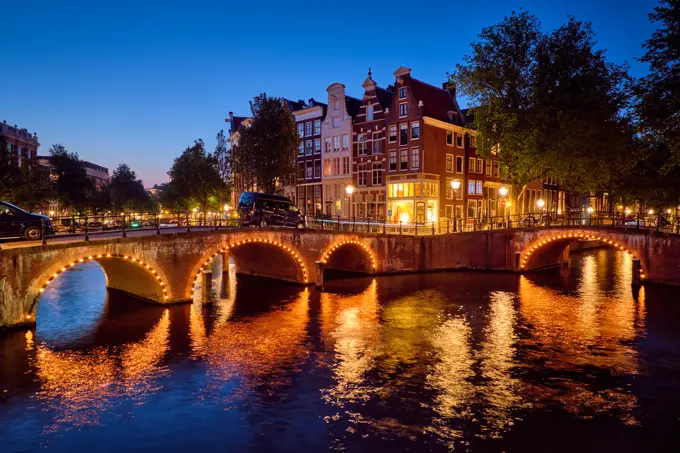 Night view of Amterdam cityscape with canal, bridge and medieval houses in the evening twilight illuminated. Amsterdam, Netherlands