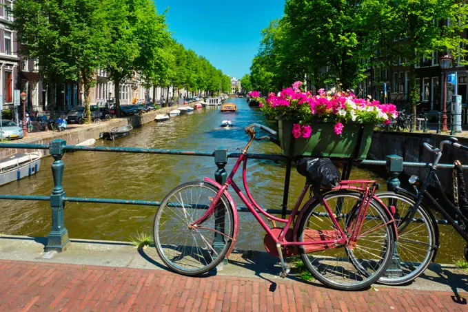 Typical Amsterdam view - Amsterdam canal with boats and parked bicycles on a bridge with flowers. Amsterdam, Netherlands