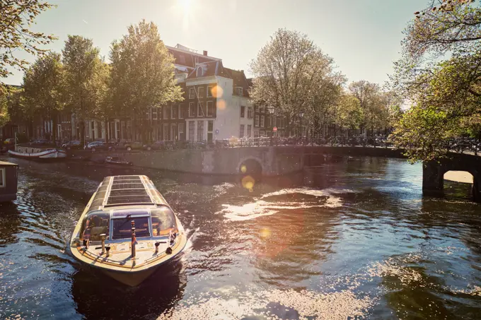 Amsterdam canal with tourist boat and old houses on sunset. Amsterda, Netherlands