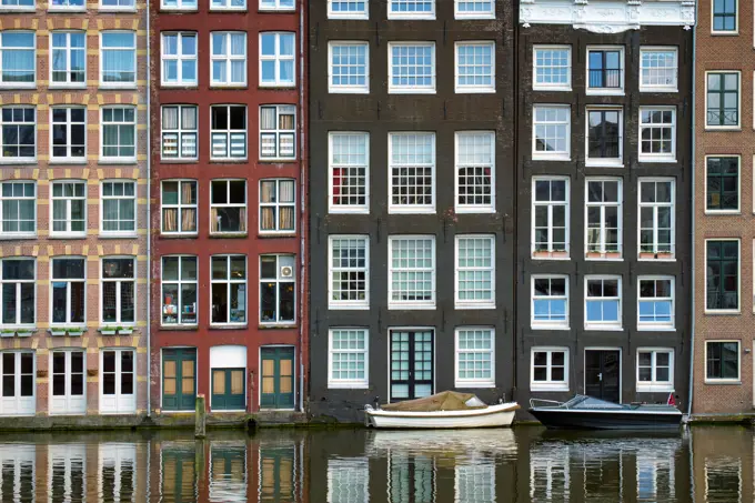 Row of typical houses and boat on Amsterdam canal Damrak with reflection. Amsterdam, Netherlands