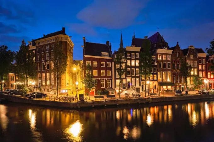 Night view of Amsterdam cityscape with canal and medieval houses in the evening twilight illuminated. Amsterdam, Netherlands