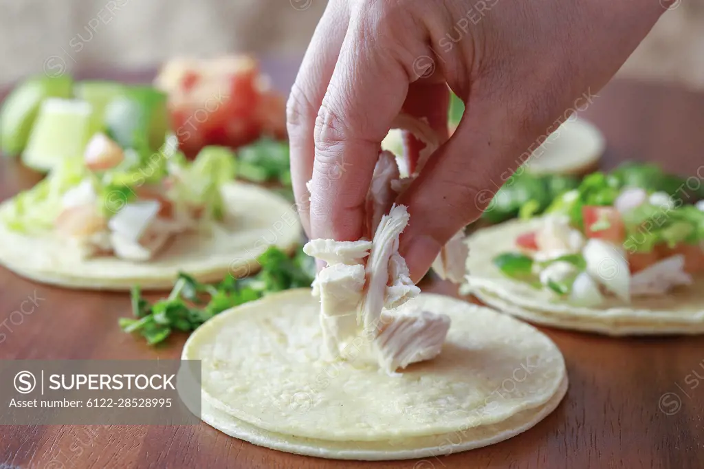 Putting pieces of chicken on a small street taco on a wooden board.