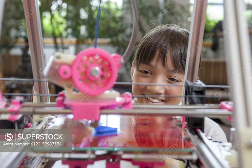 A young girl watches as a 3D printer prints an object.