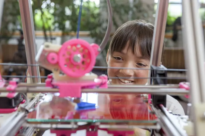 A young girl watches as a 3D printer prints an object.