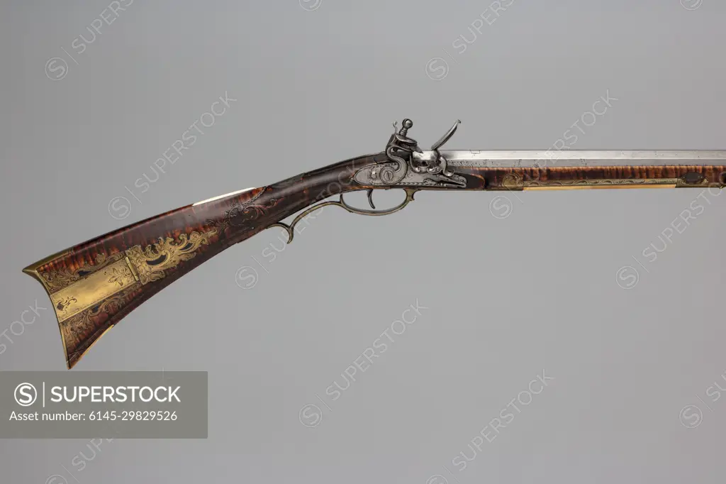 Flintlock Longrifle ca. 1810-20 Jacob Kuntz American Jacob Kuntz ranks among the most artistically accomplished and longest living American longrifle makers. Recognized as one of his finest rifles, this example is characterized by its gracefully architected stock adorned with beautifully designed and engraved metal mounts and carvings. The curved upper and lower profile of the buttstock is typical of the Lehigh Valley area of eastern Pennsylvania, where Kuntz lived and worked before he moved to Philadelphia in 1810. The carving is a testament to his comfort and skill with popular rococo ornament, as is the lively and imaginative design of the engraved brass patch box cover.. Flintlock Longrifle. American, Philadelphia. ca. 1810-20. Wood (maple), steel, iron, brass, silver, bone, horn. Philadelphia, Pennsylvania. Firearms-Guns-Flintlock