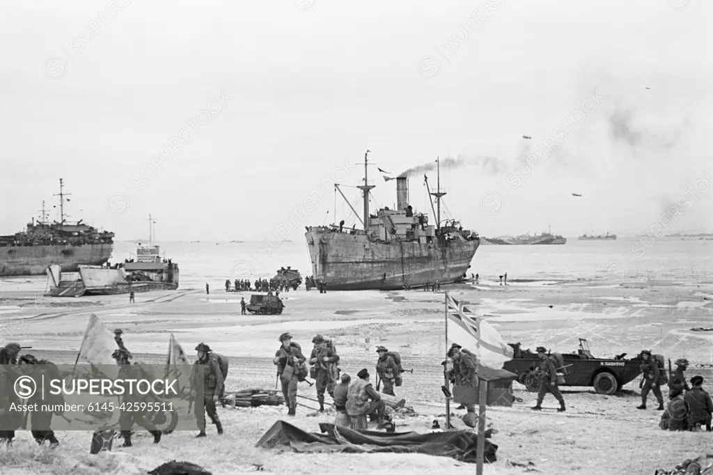 Troops come ashore on one of the Normandy invasion beaches, past the White Ensign of a naval beach party, 7 June 1944. D-Day, 6 June 1944: The White Ensign of a Naval Beach Party flying on the Normandy Coast as British troops move inland from the beached landing craft.