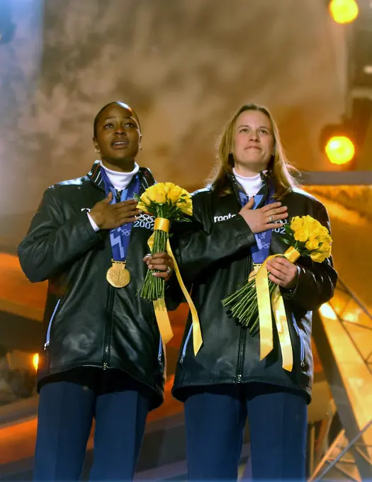 Vonetta Flowers, left, and World Class Athlete SPECIALIST Jill Bakken, USA, listen to the United States national anthem during the medal ceremony in Salt Lake City, after winning the gold medal in women's two-man bobsled for the United States in the 2002 WINTER OLYMPIC GAMES. The team was not favored going in but ended up breaking a 46 year drought for the United States, winning the Gold over another American team and favored German team, setting a track record in the process. Subject Operation/Series: 2002 WINTER OLYMPIC GAMES Base: Salt Lake City State: Utah (UT) Country: United States Of America (USA)