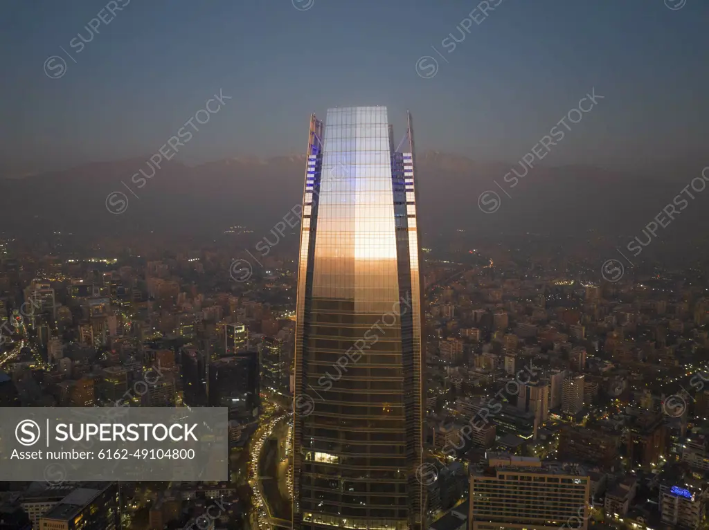 Aerial View Of Sunset Reflecting Off Tall Skyscraper With Cityscape And Andes Mountain Range In Distance, Santiago, Chile.