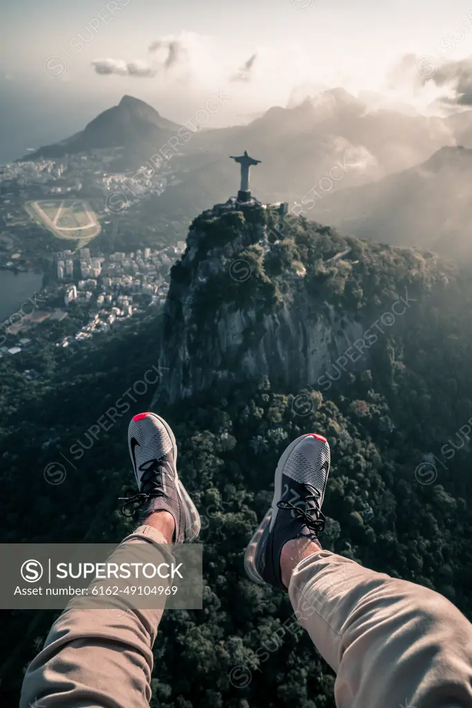 RIO DE JANEIRO, BRAZIL - 22 OCTOBER 2018: Aerial View From Helicopter Of Legs Hanging Out Over Christ The Redeemer Statue And Corcovado Mountain In City Of Rio De Janeiro, Brazil