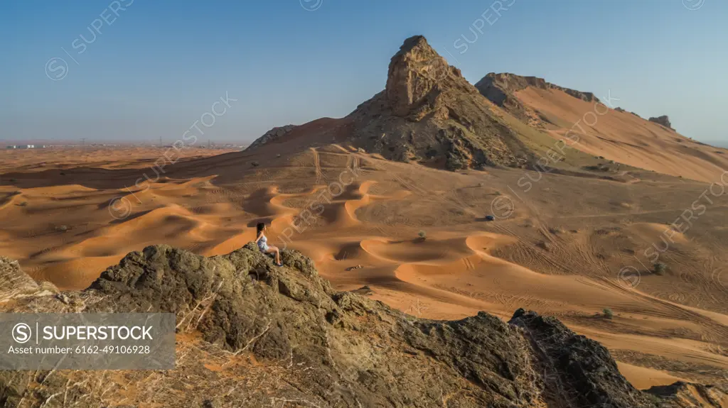 Aerial view of a girl on the top of a rocky mountain in the Camel Rock Desert Safari in UAE.