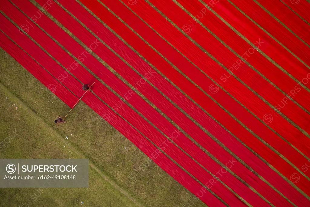 Aerial view of two people working in a field stretching red cloth in Narsingdi, Dhaka, Bangladesh.