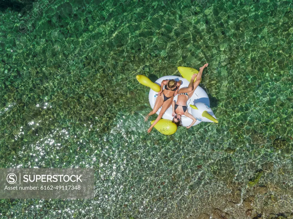 Aerial view of two women in bikinis floating on inflatable animal mattress in Panagopoula, Greece.