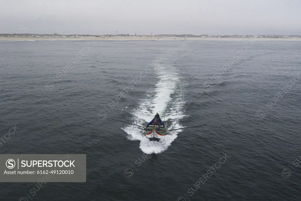 Aveiro, Portugal - 08 August 2020: Aerial view of fishermen sailing with a traditional fishing boat and doing Arte Xavega in Torreira, Portugal.