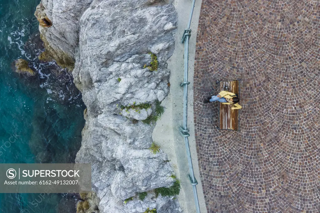 Aerial view of a woman sitting on the bench at waterfront in Erchie, Amalfi Coast, Salerno, Campania, Italy.