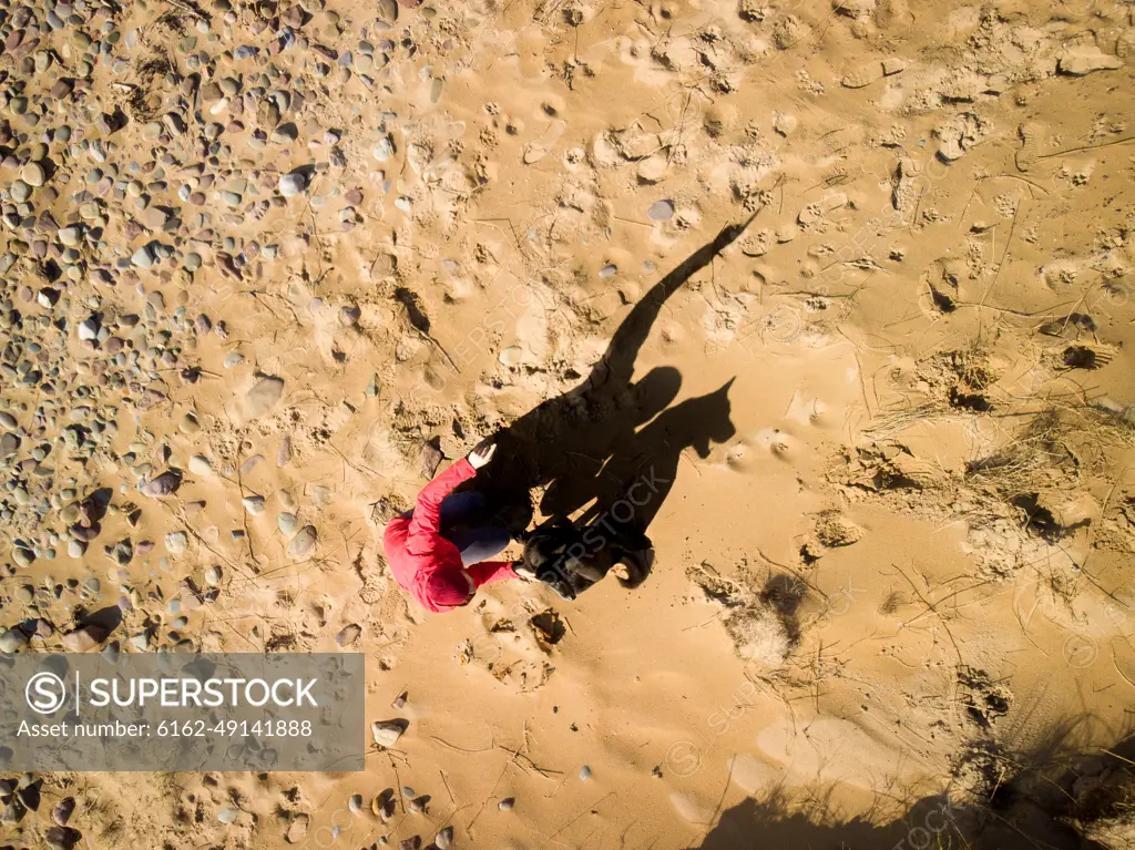 Aerial silhouette of a man with his dog,  in the afternoon sun, on Freshwater West Beach, Pembrokeshire Coast, Wales, UK