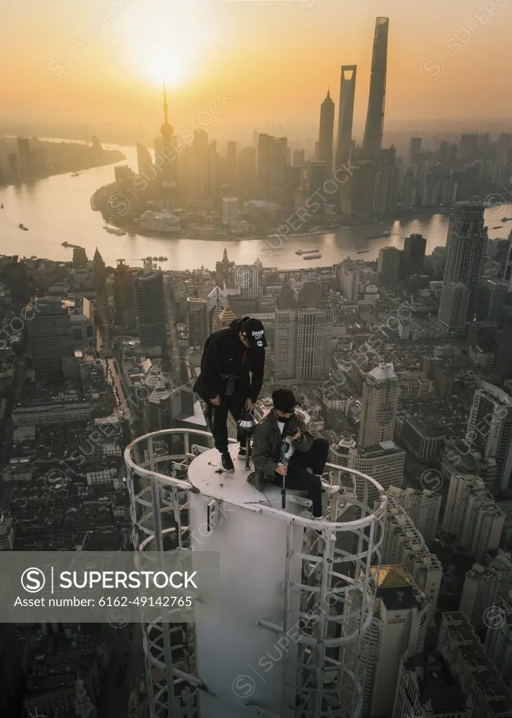 Shanghai, China - 27 April 2019: Aerial view of two young guys standing on the top of a skyscraper with Shanghai with city skyline in background at sunset, Shanghai, China.