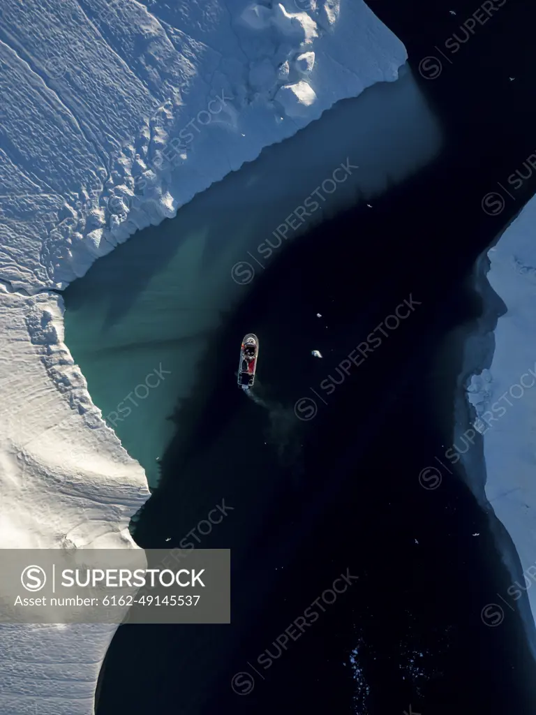 Aerial top-down drone view a red boat driving between icebergs, Ilulissat, Greenland, Arctic.