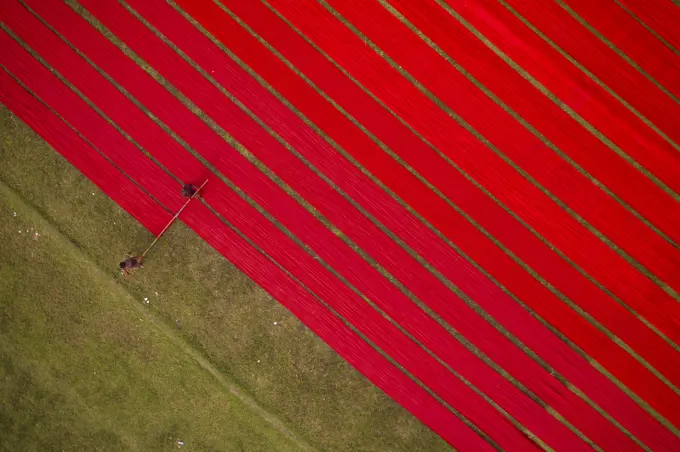 Aerial view of two people working in a field stretching red cloth in Narsingdi, Dhaka, Bangladesh.