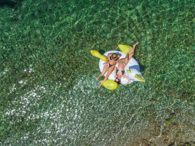 Aerial view of two women in bikinis floating on inflatable animal mattress in Panagopoula, Greece.