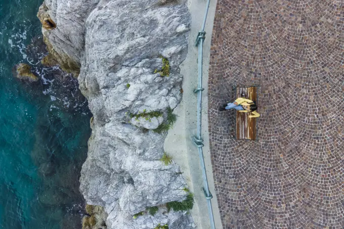 Aerial view of a woman sitting on the bench at waterfront in Erchie, Amalfi Coast, Salerno, Campania, Italy.