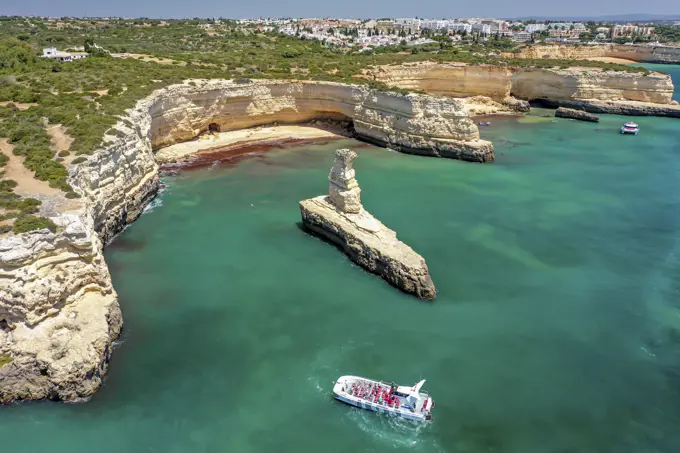 Portugal, Albufeira - 29 May 2021: Aerial view of the rocky coastline and coves with a boat on the turquoise waters of Albufeira, Algarve, Portugal.