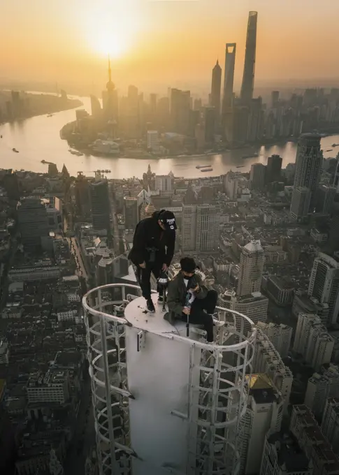 Shanghai, China - 27 April 2019: Aerial view of two young guys standing on the top of a skyscraper with Shanghai with city skyline in background at sunset, Shanghai, China.