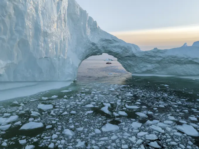 Aerial drone view of a red boat though a huge iceberg arch, Ilulissat, Greenland, Arctic.