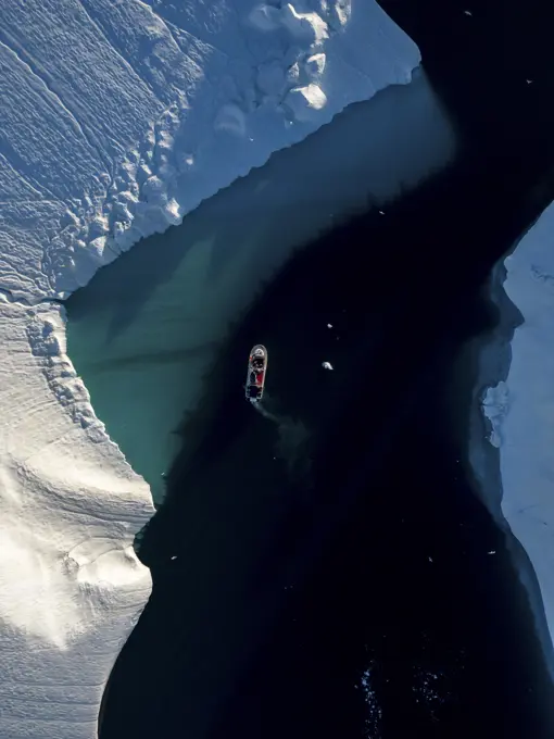 Aerial top-down drone view a red boat driving between icebergs, Ilulissat, Greenland, Arctic.