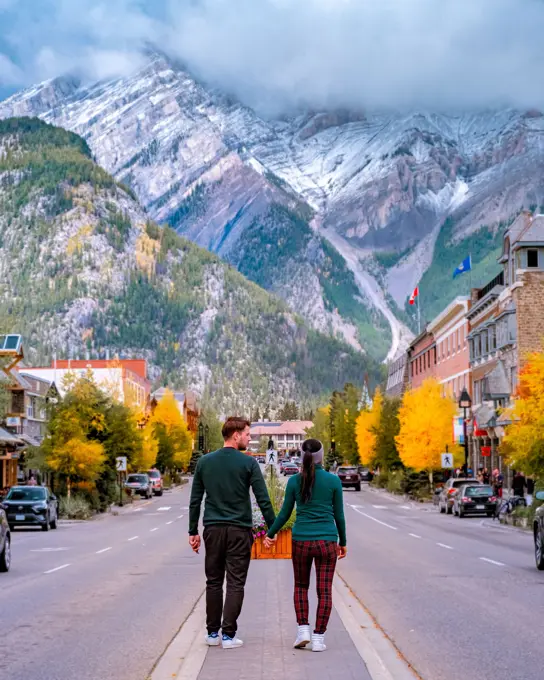 a couple visits the town of Banff Alberta Canada, couple of men, and woman walking at the street of Banff with huge rocky mountains at the background in Canada.