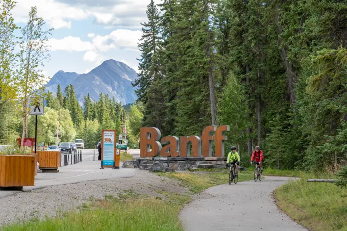 Banff Town Sign in summer time. Tourist cycling in Banff Legacy Trail. Banff National Park, Canadian Rockies.