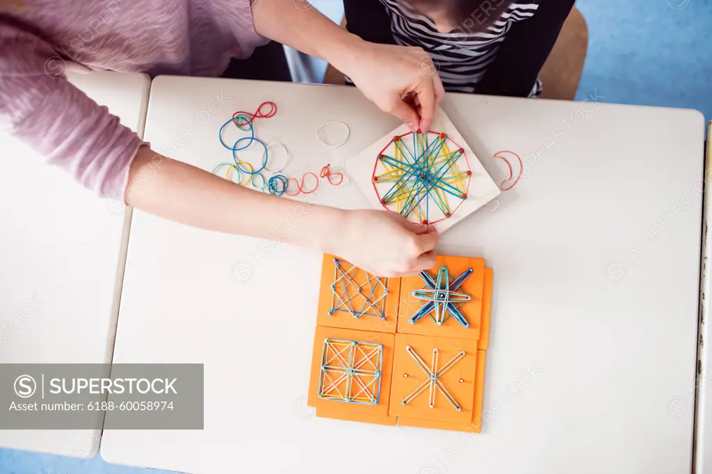 Top view of teacher using geoboard in class, teaching students, explaining geometry, shapes, fractions or patterns. Using education tools in elementary school. Top view of teacher using geoboard in class, teaching students, explaining geometry, shapes, fractions or patterns. model released