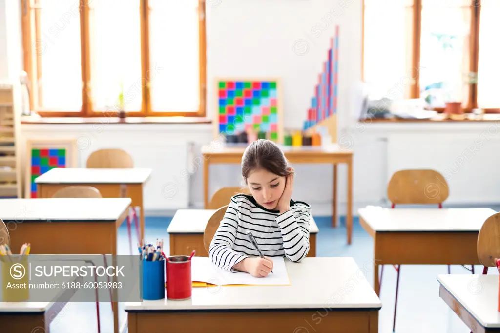 Schoolgirl, pupil sitting at desk in classroom at the elementary school. Student girl pen, writing in exercise book, notebook. Schoolgirl, pupil sitting at desk in classroom at elementary school. Student girl pen, writing in exercise book, notebook. model released