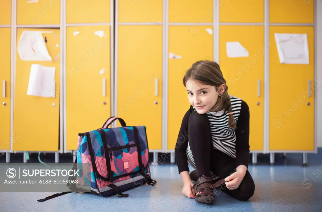 Portrait of schoolgirl, putting shoes on by lockers. Student girl with bag in hallway, after last day in elementary school before summer break. Portrait of cute schoolgirl, putting shoes on by lockers. Student girl with bag in hallway, after last day in elementary school before summer break. model released