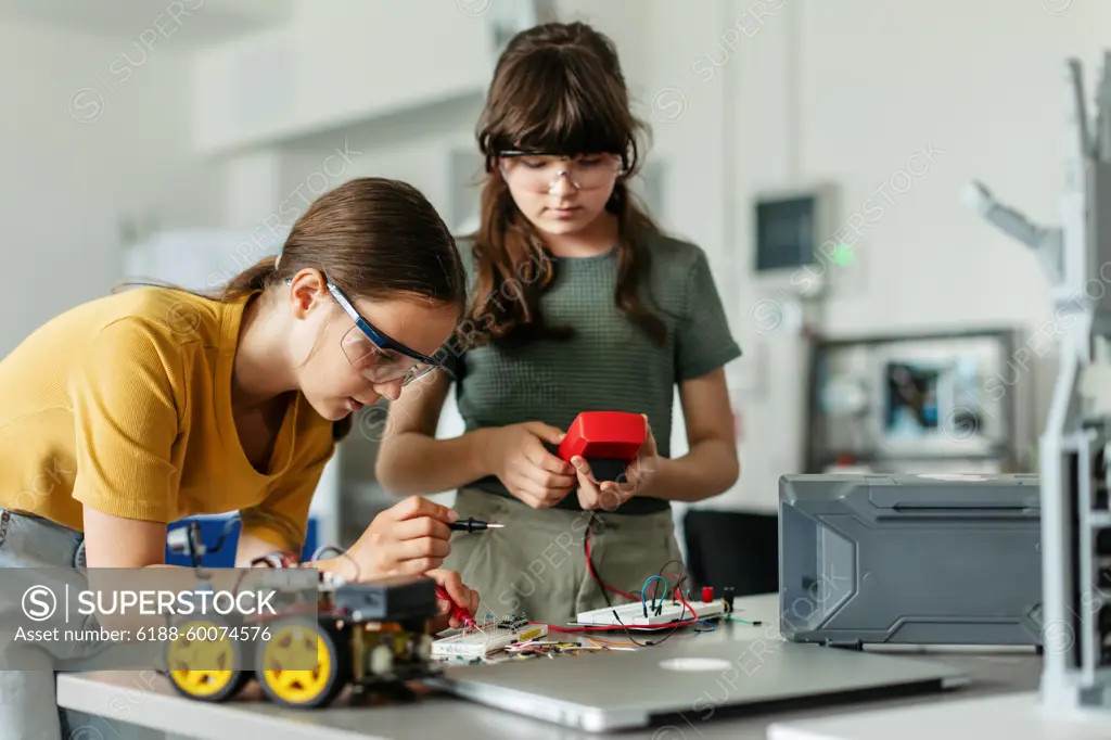 Two girl classmates working togeter on circuit board, building robotic car in after-school robotics club. Children learning robotics in Elementary school. Two girl classmates working togeter on circuit board, building robotic car in an after-school robotics club. Children learning robotics in Elementary school. model released