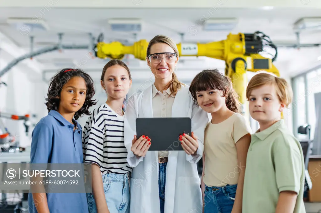 Portrait of children learning robotics in Elementary school, standing with female teacher. After-school robotics club, or field trip to real robotics laboratory. Portrait of children learning robotics in Elementary school, standing with female teacher. Young students building robot in after school robotics club. Field trip to real robotics laboratory. model released