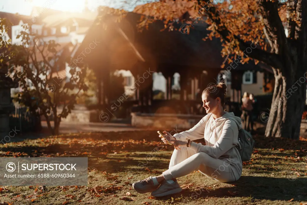 Young Fashionable Teenage Girl With Smartphone In Europian Park In Autumn Sitting At Smiling. Trendy Young Woman In Fall In Park Texting. Retouched, Vibrant Colors. Beautiful Blonde Teenage Girl Wearing Casual Modern Autumn Outfit Sitting In Park In Autum Young fashionable teenage girl with smartphone in park in autumn sitting at smiling. Trendy young woman in fall in park texting. Retouched, vibrant colors. Beautiful blonde teenage girl wearing casual modern autumn outfit sitting in park in autumn. Retouched, vibrant colors, brownish tones. Copyright: xZoonar.com/AlexxPopovx 21853797