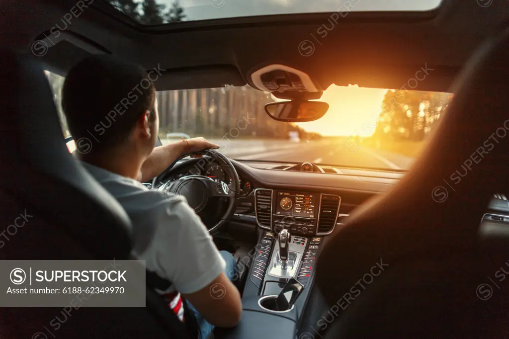 Mann in einem Premium-Auto mit einem Interieur fährt bei Sonnenuntergang. Konzept Reisen mit dem Auto *** Man in a Premium Car with a Interior drives at Sunset Concept Travel with the Car 1102809359 ,model released, Symbolfoto