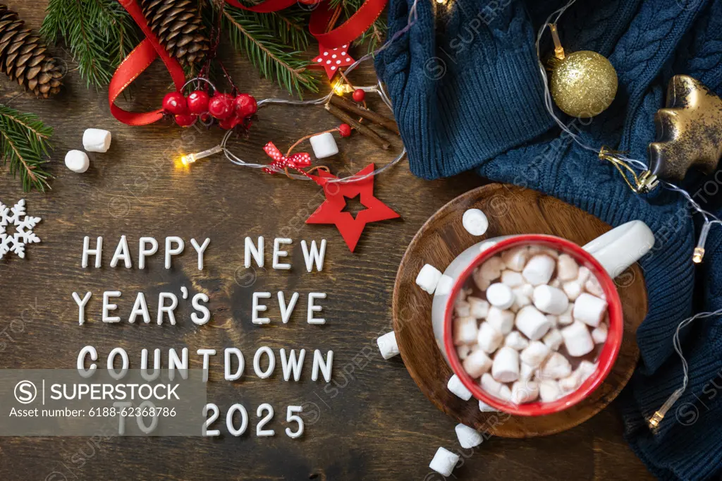 Winter, christmas lights, cozy cup hot chocolate drink with marshmallow on wooden table background. View from above with english text Happy New Year s Eve countdown to 2025. Winter, christmas lights, cozy cup hot chocolate drink with marshmallow on wooden table background. View from above with english text Happy New Year s Eve countdown to 2025. Copyright: xZoonar.com/ELENAxHRAMOVAx 22077028