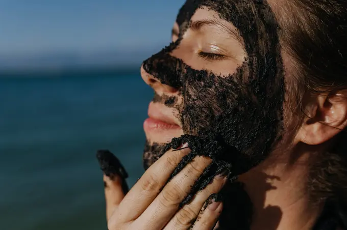 Woman applies healing mud to her face and body. Natural healing mud in Croatia on the beach. Woman applies healing mud to her face and body. Natural healing mud in Croatia on the beach. Therapeutic mud or peloids rich in minerals and organic substances. model released