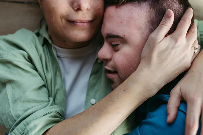 Portrait of young man with Down syndrome with his mother at home, holding, touching with foreheads. Concept of love and parenting disabled child. Close up. Portrait of young man with Down syndrome with his mother at home, holding, touching with foreheads. Concept of love and parenting disabled child. Close up shot. model released