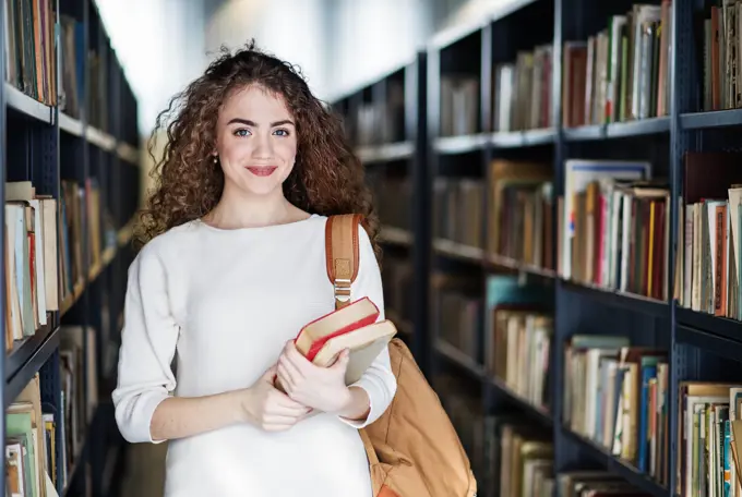 Young female student in library, looking for books, preparing for final exam. Young female student in library, looking for books, preparing for final exam. Books, textbooks, journals on shelves in university library. model released