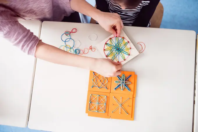 Top view of teacher using geoboard in class, teaching students, explaining geometry, shapes, fractions or patterns. Using education tools in elementary school. Top view of teacher using geoboard in class, teaching students, explaining geometry, shapes, fractions or patterns. model released