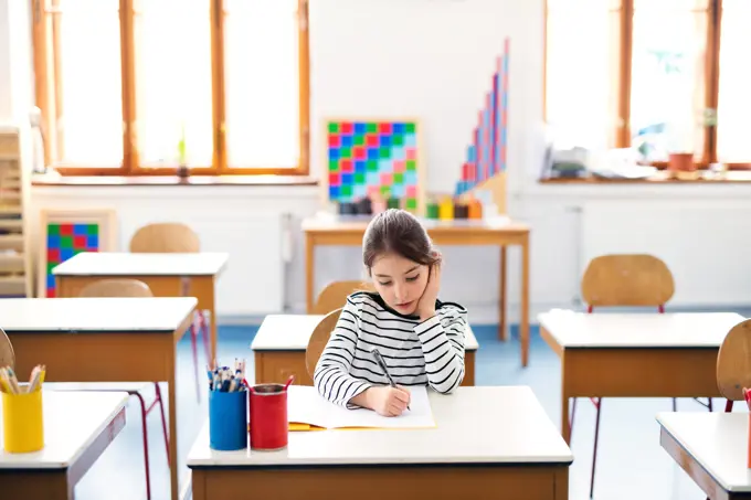 Schoolgirl, pupil sitting at desk in classroom at the elementary school. Student girl pen, writing in exercise book, notebook. Schoolgirl, pupil sitting at desk in classroom at elementary school. Student girl pen, writing in exercise book, notebook. model released