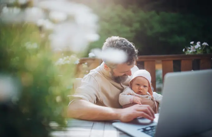 Dad working from homeoffice, sitting on patio with laptop, holding little baby girl. Father spending time with small daughter, enjoying together time. Father s Day. Dad working from homeoffice, sitting on patio with laptop, holding little baby girl. Father spending time with small daughter, enjoying together time. Father s Day concept. model released