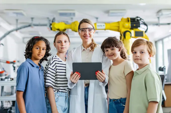 Portrait of children learning robotics in Elementary school, standing with female teacher. After-school robotics club, or field trip to real robotics laboratory. Portrait of children learning robotics in Elementary school, standing with female teacher. Young students building robot in after school robotics club. Field trip to real robotics laboratory. model released