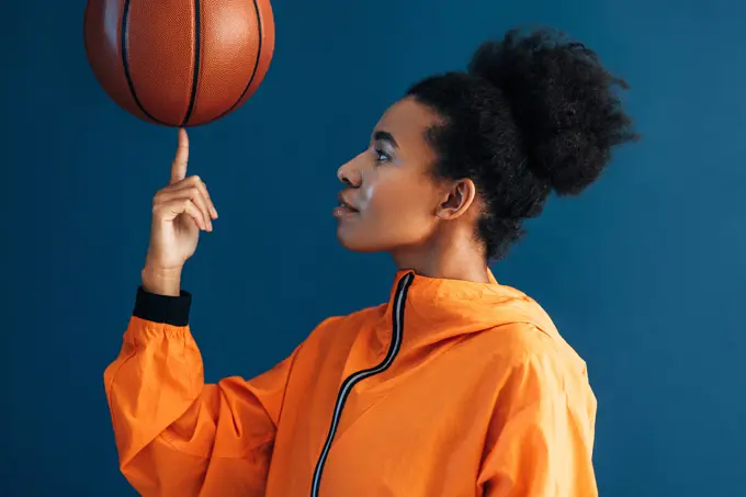 Side view of young woman with curly hair holding basketball on finger. Studio shot of female basketball player posing in studio. Side view of young woman with curly hair holding basketball on finger. Studio shot of female basketball player posing in studio. Copyright: xxArtemxVarnitsinx