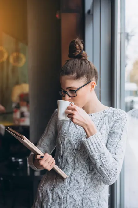 Young girl looking at tablet and smiling in cafe with big window. Young girl looking at tablet and smiling in cafe with big window. She has beverage in hand ,model released, Symbolfoto Copyright: xZoonar.com/OleksiixHrecheniukx 11801286 ,model released, Symbolfoto ,property released