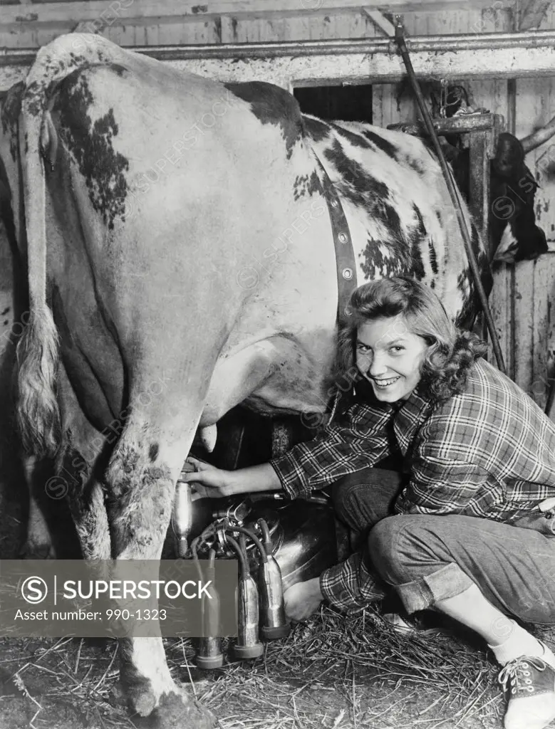 Portrait of a young woman milking a cow with a milking machine